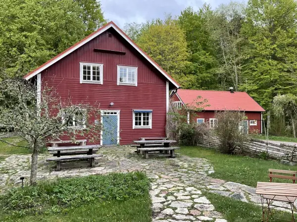Stocklycke vandrarhem, röda trähus med vita knutar och fönster, omgivna av grönskande skog. Picknickbord och stenlagd uteplats inbjuder till avkoppling.