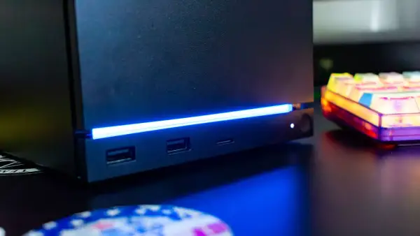 Czarny steam machine z niebieskim podświetleniem, portami USB i gniazdem na kartę SD. Obok kolorowa klawiatura.