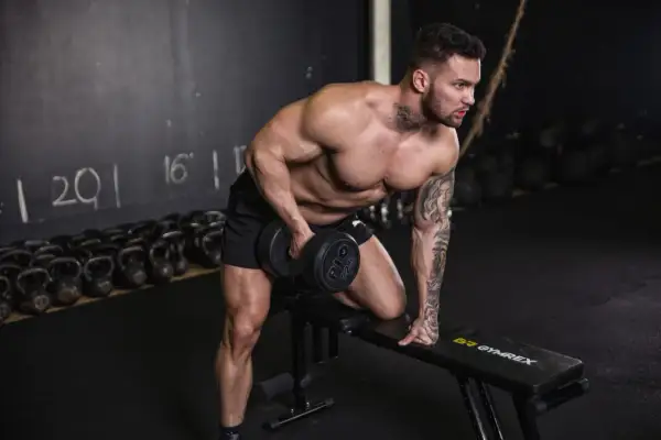Mann macht ein Workout mit Hanteln auf einer Bank im Fitnessstudio.