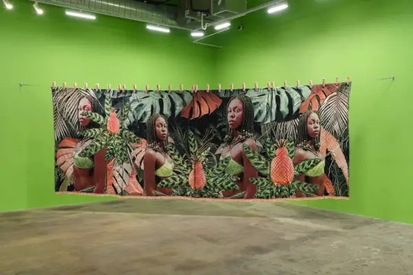A tapestry at little April Galleries features four portraits of women amidst lush tropical foliage and pineapples.