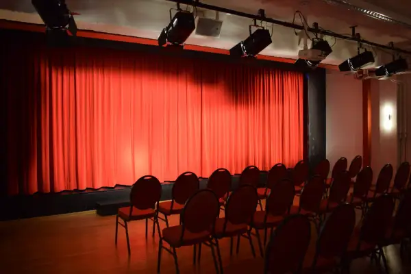 Rote Vorhänge und leere Stühle im **theas theater**. Scheinwerfer sind an der Decke montiert, bereit für die nächste Vorstellung.