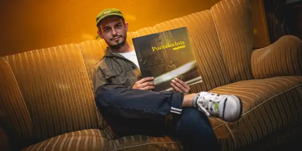 Młody mężczyzna w czapce z daszkiem siedzi na kanapie, trzymając w rękach płytę Vito Bambino "Poczekalnia".