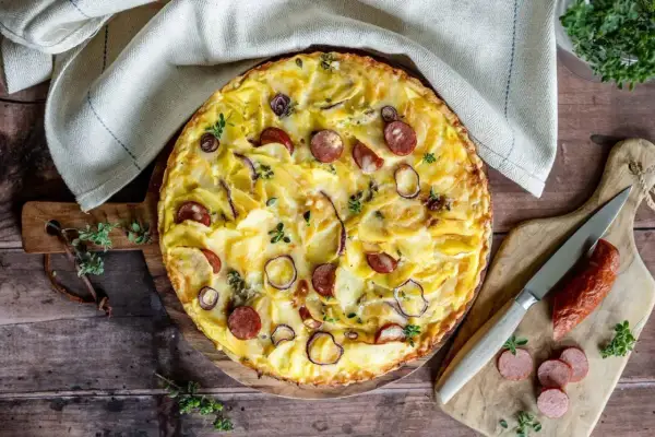 Herzhafte Kartoffeltorte mit Speck und Zwiebeln, goldbraun gebacken und mit frischen Kräutern garniert. Ein Genuss für jeden Anlass.