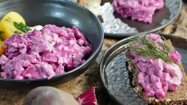 Omas roter Heringssalat, cremig und leuchtend pink, serviert mit Kartoffeln und auf Brot mit Dill.