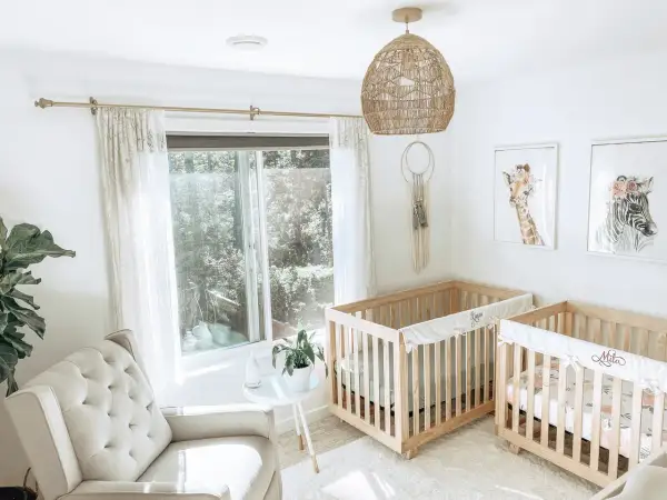 A serene twin m nursery with two wooden cribs, a plush armchair, and whimsical animal art.