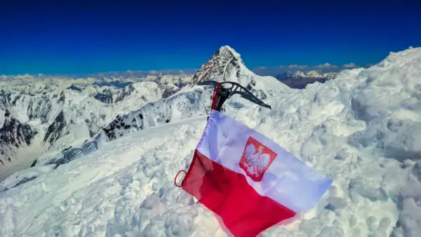 Na śnieżnym szczycie, z lodową siekierą i polską flagą, rozpościera się widok na skalisty, szeroki szczyt i góry.
