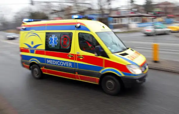 Żółto-czerwono-niebieska karetka Medicover z włączonymi sygnałami świetlnymi, w ruchu. Charakterystyczne oznaczenia karetek na karoserii.
