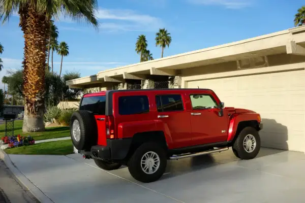 Czerwony Hummer H3 zaparkowany przed domem z palmami w tle.