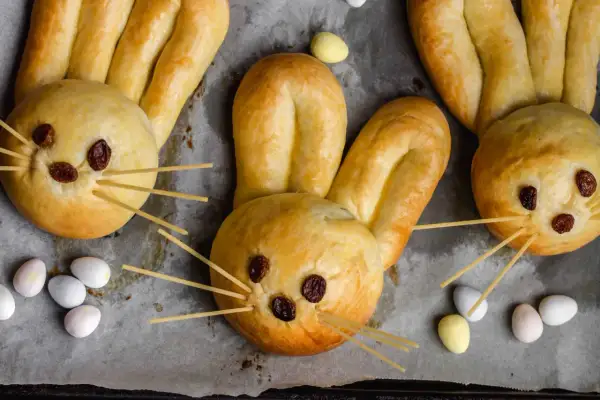 Osterhasen backen mit Hefeteig: Süße Hasen aus Teig mit Rosinenaugen und Spaghetti-Schnurrhaaren, umgeben von bunten Ostereiern.