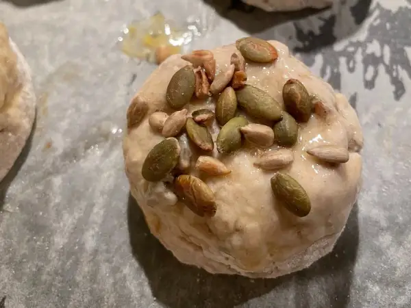 Nybakade glutenfria frallor med pumpa- och solrosfrön på en bakplåt.