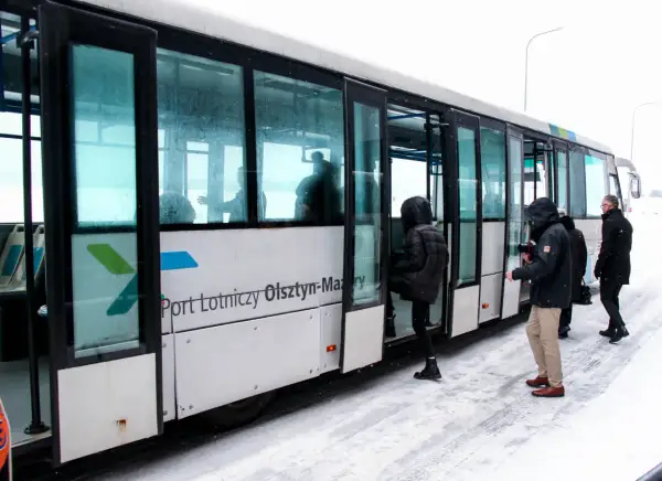 Szynobus z napisem "Port Lotniczy Olsztyn-Mazury" na tle śniegu, z pasażerami wsiadającymi.