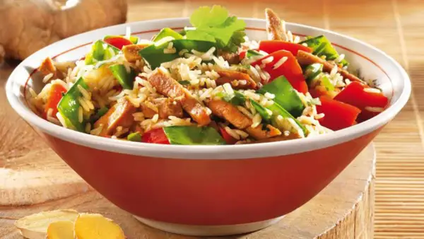 Schüssel mit Reis, Fleischstreifen, Paprika und Erbsen. Ein köstliches Gericht aus der Wok-Küche, garniert mit Koriander.