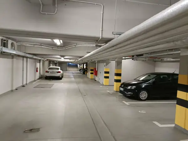 Wrocław główny parking cennik: podziemny parking z białym i czarnym Volkswagenem, białym BMW, rurami i klimatyzacją.