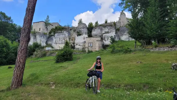Kobieta z rowerem na tle ruin zamku na wapiennych skałach. Piękny dzień na trasie rowerowy szlak orlich gniazd.