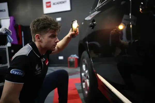 Detailer używa lampy, by ocenić stan lakieru. Widać drobne niedoskonałości na czarnym samochodzie.