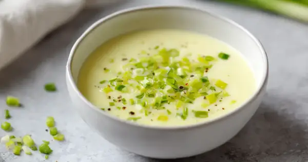 Un bol de fondue de poireaux crémeuse, garnie de poireaux frais hachés et de poivre noir.