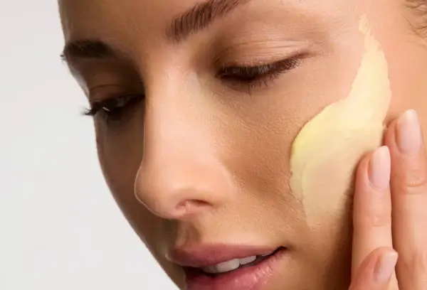 Application d'une crème riche en céramides pour une peau éclatante. Les doigts doux étalent la texture onctueuse.