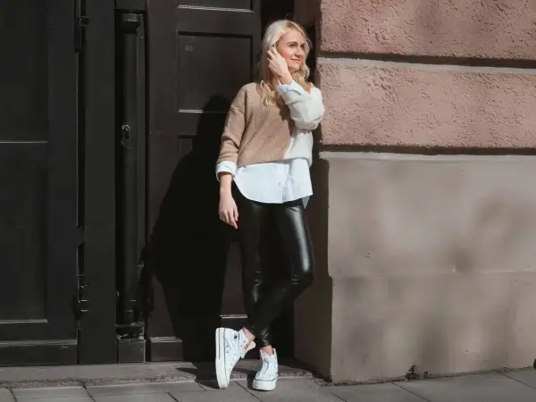 Styling-Tipp: So kannst du lederleggings kombinieren. Eine Frau mit blonden Haaren trägt sie mit einem weißen Hemd und einem zweifarbigen Pullover.