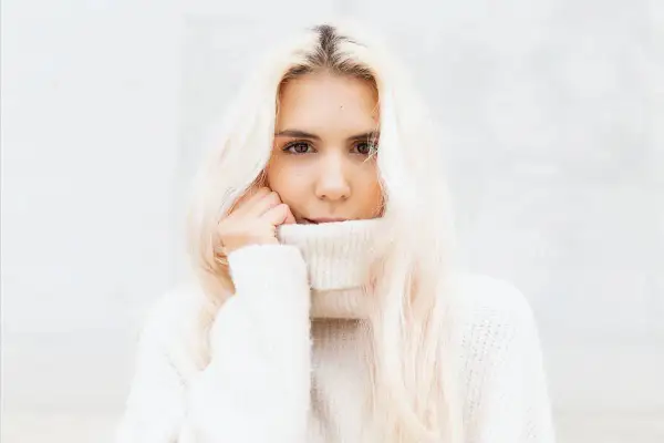 Blondynka w białym golfie, z włosami opadającymi na ramiona, wygląda jak uosobienie stylu vanilla girl.
