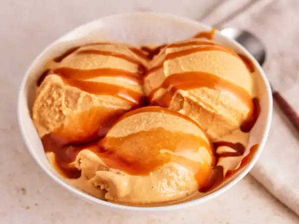 Drei Kugeln cremiges Karamell-Eis, übergossen mit flüssigem Karamell, in einer weißen Schüssel.