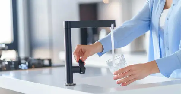 Une personne remplit un verre d'eau du robinet, peut-être pour tester la dureté de l'eau.