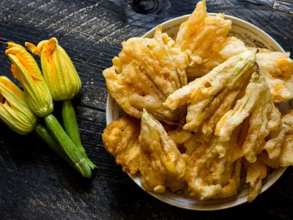 Flores de calabacín frescas y doradas flores de calabacín rebozadas en un plato.
