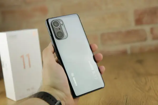 Dłoń trzyma błyszczący telefon Xiaomi 11i z potrójnym aparatem. Obok stoi białe pudełko z cyfrą 11.