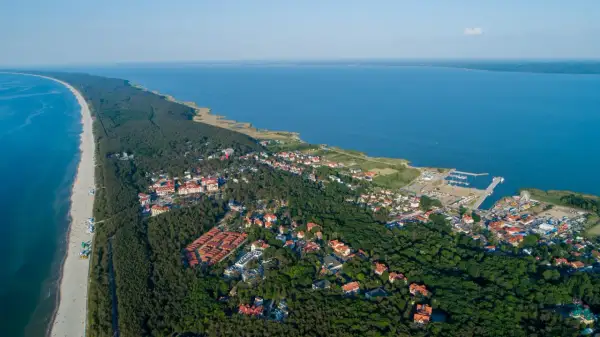 Widok z lotu ptaka na Krynicę Morską. Widoczne plaże, lasy, zabudowania i port. Mnóstwo atrakcji czeka na turystów.