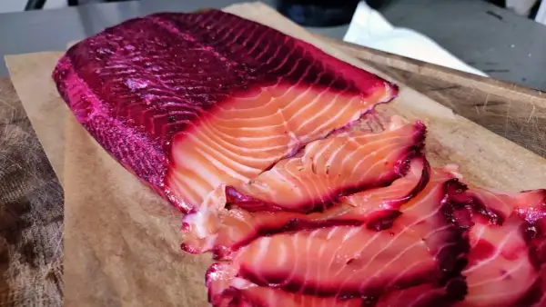 Rote Bete Lachs, mariniert und in Scheiben geschnitten, liegt auf Backpapier. Die leuchtend pinken Ränder des Lachses sind ein Blickfang.