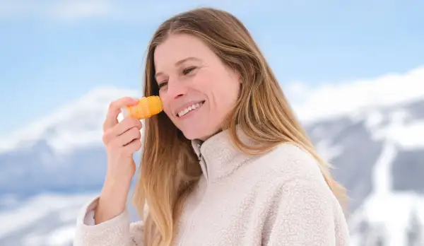 En hiver, faut-il mettre de la crème solaire ? Cette femme souriante en applique sur son visage, profitant d'un paysage enneigé.
