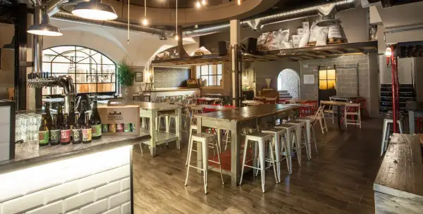 Interno del birrificio Legnano con tavoli, sgabelli e birre in bottiglia sul bancone.