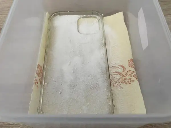 Przezroczyste etui na telefon zasypane sodą oczyszczoną, przygotowane do czyszczenia. To prosty sposób, jak wyczyścić zżółknięte etui.
