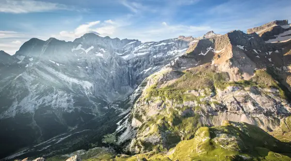 Le cirque de Gavarnie, majestueux amphithéâtre naturel, dévoile ses falaises abruptes, une cascade lointaine et des pentes verdoyantes sous un ciel bleu.