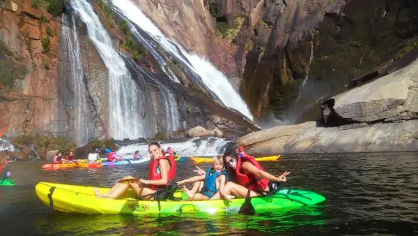 Familia disfrutando en kayak frente a la impresionante fervenza de Ézaro, con cascadas cayendo sobre rocas.