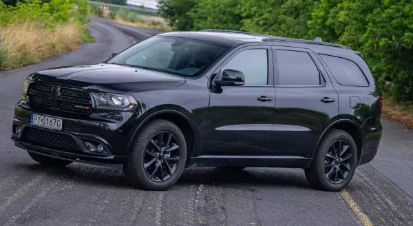 Czarny Dodge Durango 5.7 Hemi na krętej drodze, otoczony zielenią. Potężny SUV gotowy na każdą przygodę.