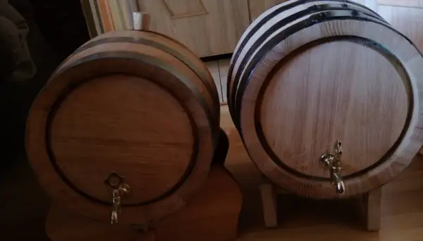 Dwa drewniane beczki, jedna z korkiem, druga z kranikiem, czekają aż coś w nich dojrzewa w dębowych beczkach.