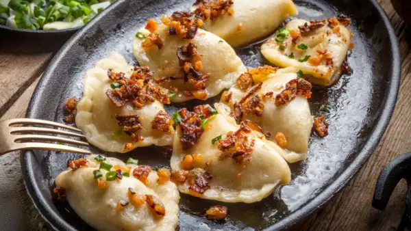 Pyszne pierogi z mięsem, posypane skwarkami i szczypiorkiem, podane na żeliwnej patelni.