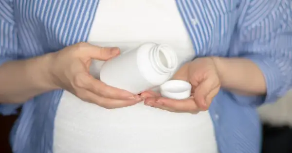 Kobieta w ciąży trzyma białą buteleczkę i jej nakrętkę. Rozważa, czy wziąć paracetamol w ciąży.