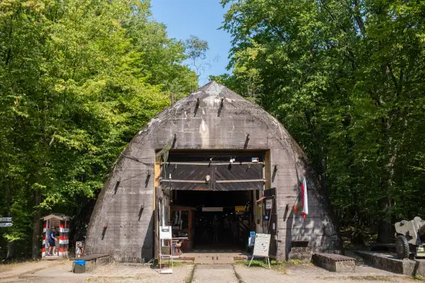 Betonowy bunkier w lesie, jedna z ciekawych województwo łódzkie atrakcje. Wejście otwarte, widać ludzi i ekspozycję.