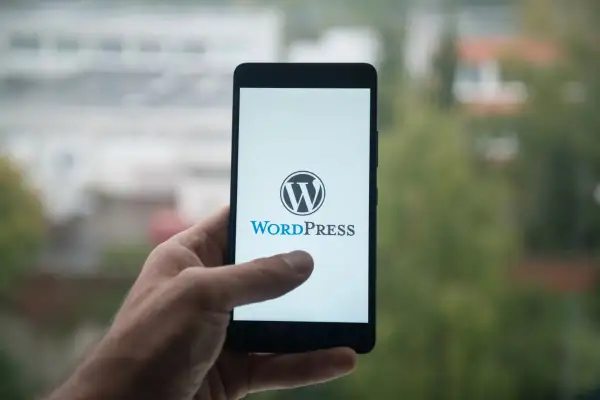 Dłoń trzyma smartfon z logo WordPress. Idealne narzędzie dla webmasterów do zarządzania stronami.