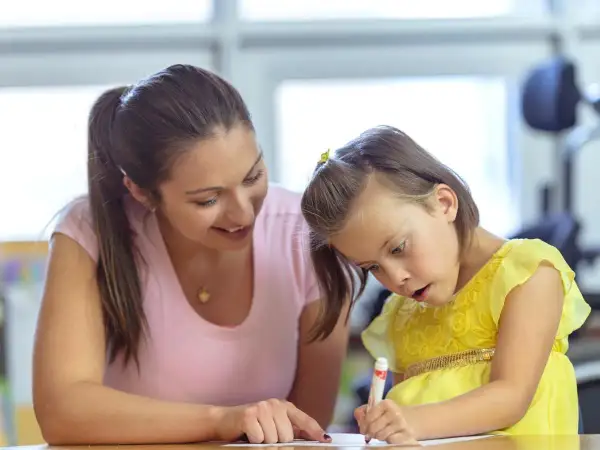 Een vrouw helpt een meisje met autisme met haar huiswerk. Ze probeert haar zin te doordrijven en te motiveren.