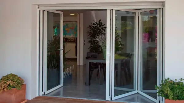 Puertas de cristales plegables que abren a un comedor interior con plantas y una mesa.