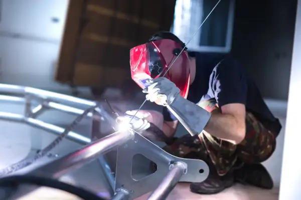 Spawacz w masce spawa aluminiową ramę. Widać jasny łuk spawalniczy i iskry. To pokazuje, czym spawać aluminium.