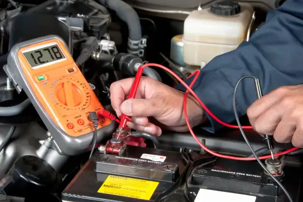 Mechaniker prüft mit Multimeter die Autobatterie, um den Anlasser wechseln zu können.