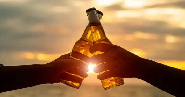 Dwie ręce wznoszą butelki piwa do toastu o zachodzie słońca. W Niemczech od ilu lat można pić alkohol? Od 16 roku życia.
