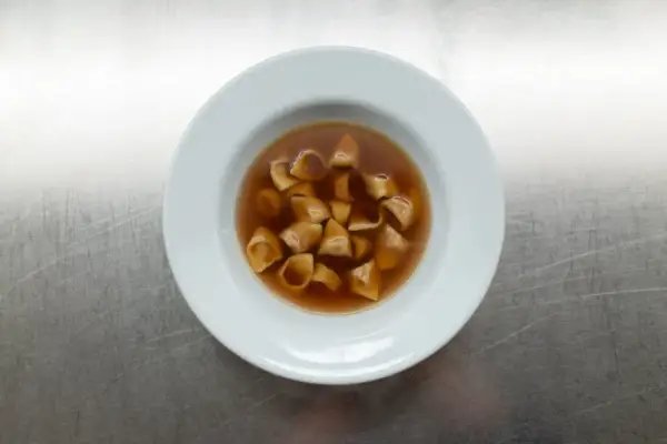 Eine Schüssel mit dampfendem Tortellini in Brodo auf einem metallischen Hintergrund.