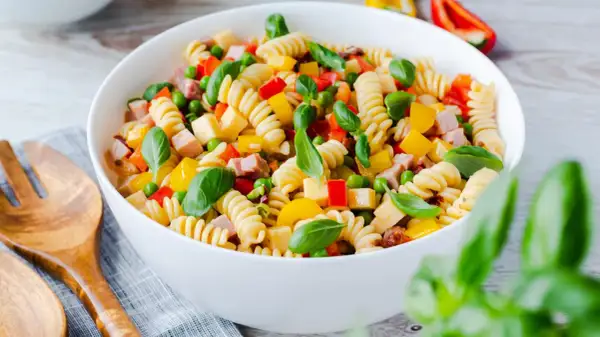 Bunter Nudelsalat ohne Mayo mit Spiralnudeln, Erbsen, Paprika und Schinkenwürfeln, garniert mit Basilikum.