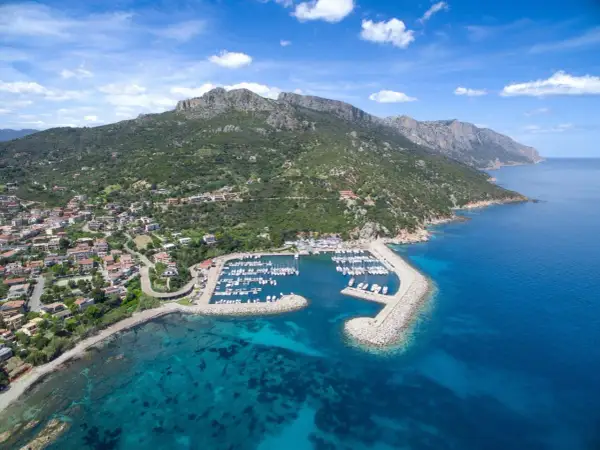 Baunei: un porto turistico con barche ormeggiate, case colorate e montagne verdi che si tuffano nel mare cristallino. Le spiagge vicine invitano al relax.