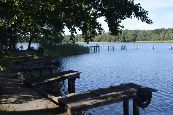 Drewniane pomosty nad spokojnym, błękitnym jeziorem Chrzypsko Wielkie. W oddali widoczne paliki i zalesiony brzeg.