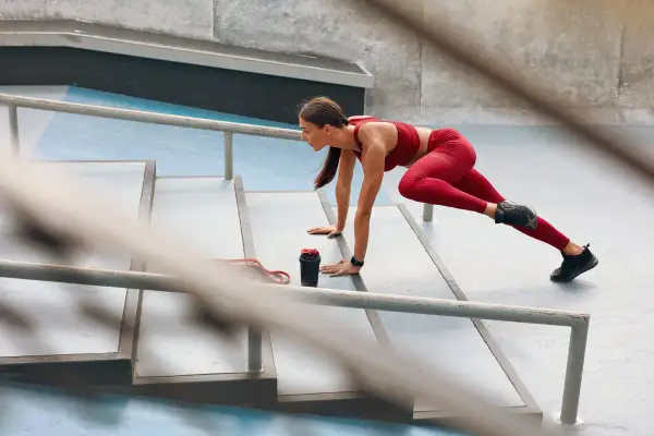 Donna in tenuta sportiva rossa esegue un esercizio per snellire le gambe senza ingrossarle, su una scalinata all'aperto.